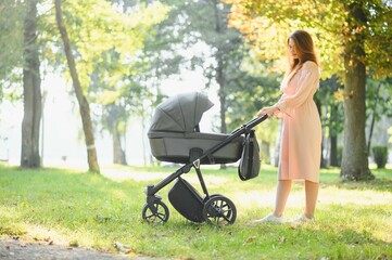 Happy young mother with baby in buggy walking in autumn park