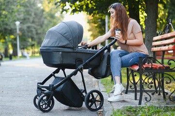 Happy young mother with baby in buggy sitting on bench in autumn park