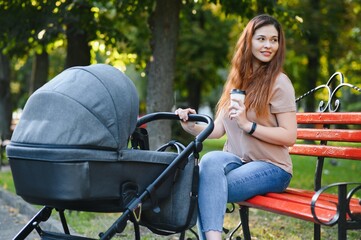 Fototapeta na wymiar Happy young mother with baby in buggy sitting on bench in autumn park