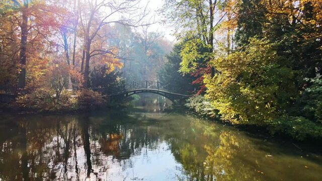 Scenic view of misty autumn landscape with beautiful old bridge the garden with red maple foliage.