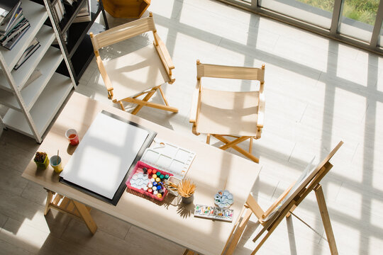 Top View Shot Of Drawing Painting Artist Hobby Workshop Studio Equipment On Wooden Table Including Canvas Easel Stand Watercolor Paintbrush Pencils Palette Tray Paper Under Strong Light From Outside