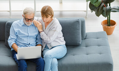 Caucasian old senior elderly lovely lover grandparents romantic couple gray hair and bearded husband and wife sitting smiling laughing watching comedy movie together on couch in living room at home