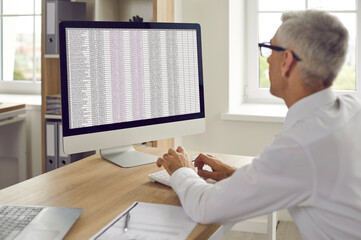 Over shoulder view of man employee work on computer in office with charts. Businessman use PC type on sheet document online. Accountant or financial manager at workplace. Finance, banking concept.