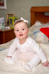 a little baby girl in a white dress is sitting on the bed