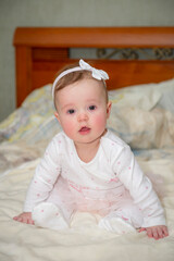 Fototapeta premium a little baby girl in a white dress is sitting on the bed