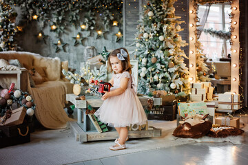 Fototapeta na wymiar A little girl in an elegant dress plays with a colorful train toy in a room decorated for Christmas