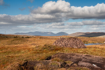 Pile of turf in a bog, Beautiful country side with tall mountains in the background. Connemara, county Galway, Ireland. Warm sunny day, cloudy sky. Traditional source of energy.
