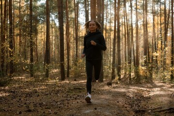 Young athletic woman jogging in forest in sunny morning. Healthy lifestyle concept.