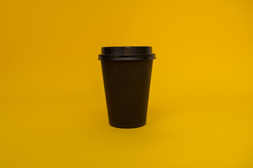 Paper black coffee cup to take away on a yellow background, black glass for tea or coffee