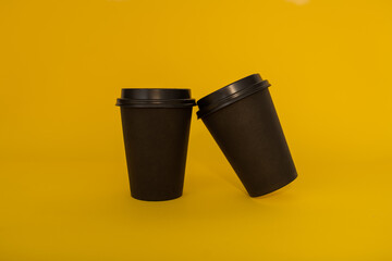 Two paper black coffee cups for takeaway on a yellow background, two black cups for tea or coffee