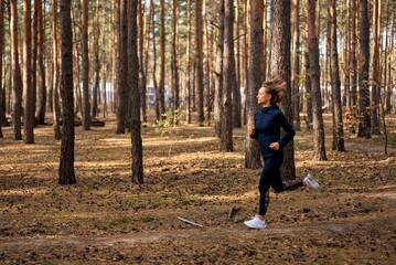 Obraz premium Young athletic woman jogging in forest in sunny morning. Healthy lifestyle concept.