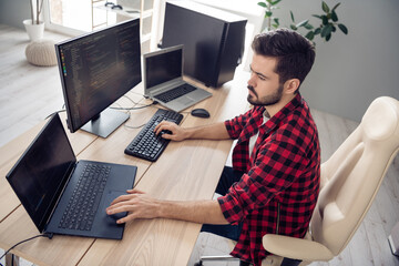 Photo of concentrated serious young man walk programmer write code pc sit table inside indoors...