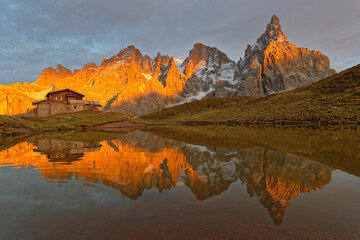 Fototapeta na wymiar PASSO ROLLE, ITALY, October 19, 2021 : Pale di San Martino Group reflecting on a lake during sunset, in Dolomites mountains.