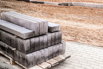 Obraz na płótnie Canvas Storage of concrete road curbs on pallets at the construction site. Curb stones prepared for installation. Finished products warehouse.