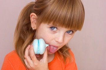 Beautiful little girl holding a blue sweet dessert macarons in her hands portrait close-up, sweet pastries happy childhood childish emotions, selective focus	