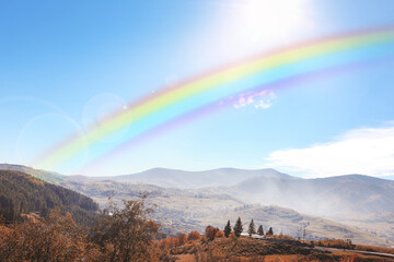 Beautiful rainbow in blue sky over mountains on sunny day