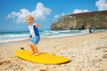 Cute blond toddler boy practice surfboard posing