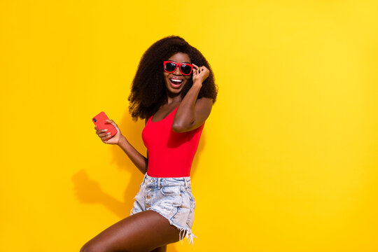 Photo of optimistic nice brunette lady hold telephone wear eyewear top shorts isolated on yellow color background