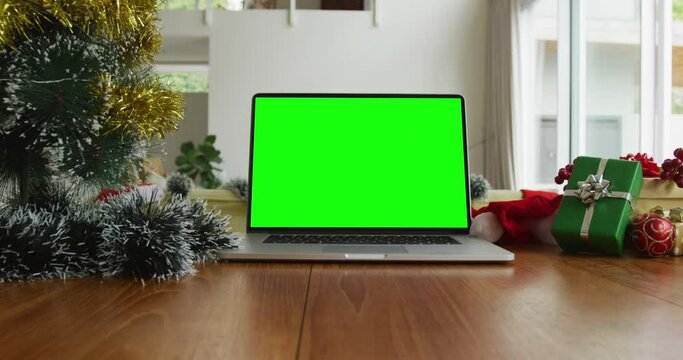 Laptop with green screen copy space on table with santa hats, christmas tree and presents