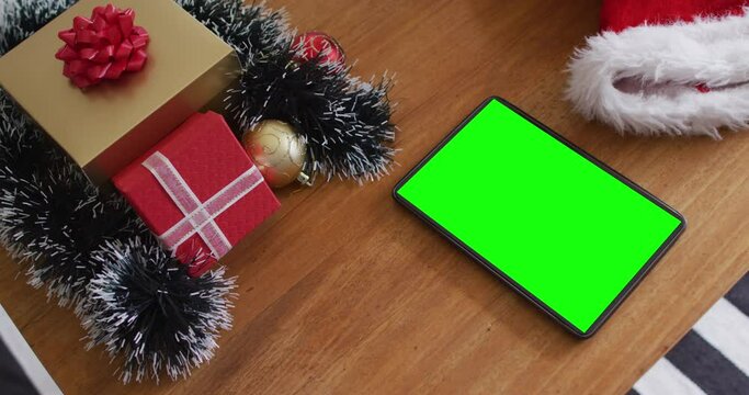 Tablet with green screen on table with santa hats and christmas presents