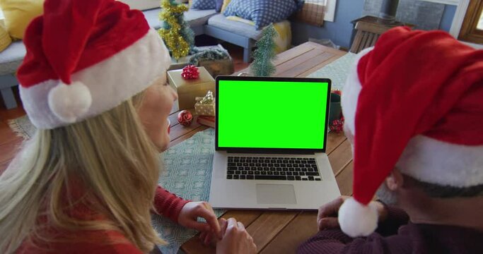 Smiling caucasian couple in santa hats making laptop christmas video call, with green screen
