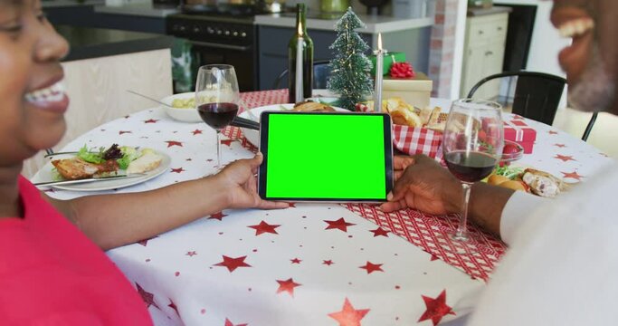 Smiling african american couple in santa hats making tablet christmas video call, with green screen