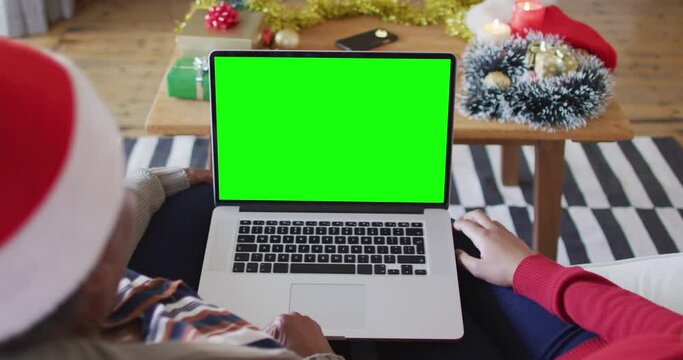 African american mother with daughter making laptop christmas video call, with green screen