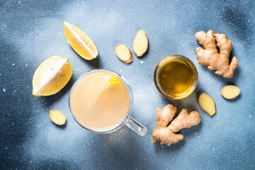 Ginger tea with lemon and honey in glass mug with ingredients. Top view at grey stone table.