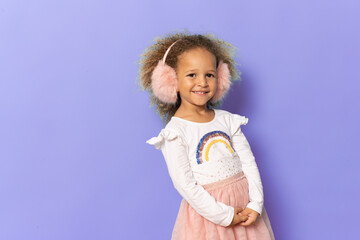 Cute little girl wearing stylish earmuffs isolated over purple background