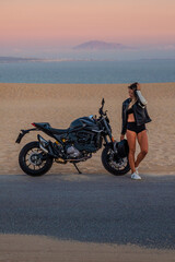 Mujer joven sexy y atlética con su moto al atardecer en las dunas de Tarifa, Cádiz, Andalucía,...