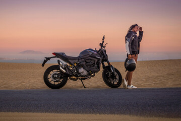 Mujer joven sexy y atlética con su moto al atardecer en las dunas de Tarifa, Cádiz, Andalucía, España