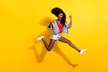 Fototapeta na wymiar Full length body size photo of girl jumping showing heavy metal sign laughing isolated bright yellow color background