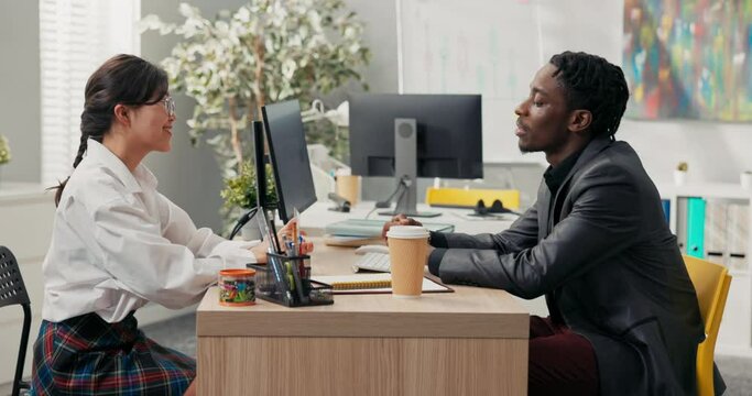 head of company, dark-skinned in suit, talks to candidate for position of office secretary girl with Asian features jokes with man they laugh job interview shaking hands to thank for meeting, goodbye