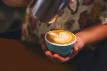 Close up barista hands making coffee latte art,Barista pouring milk in coffee mug for making latte art at cafe’