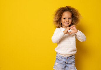 Love sign. Cute little girl makes a heart with her fingers isolated over yellow background.
