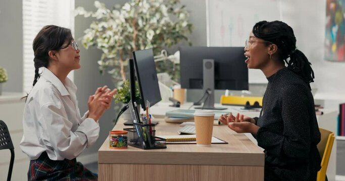 Women sit at desk across from each other job interview common language topic for gossip dark-skinned boss laughs along with candidate for position in corporate office shake hands as sign of agreement