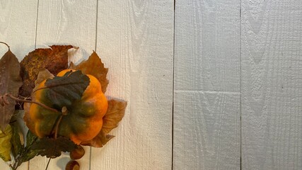 On a wooden table painted in white, the leaves are covered with a pumpkin
