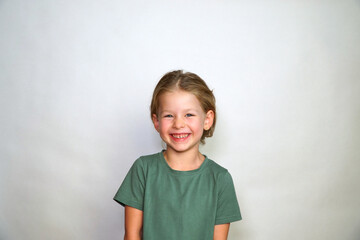 Portrait of a girl on a white background. Collected hair and green T-shirt. Cute smile happy smile. A cheerful and serious child looks at the camera. place for text.