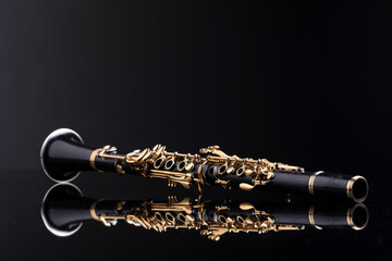 A full size clarinet with gold plated keys laying on a reflective surface with a dark background. A...