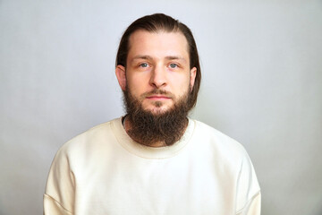 Portrait of a bearded man ON A WHITE BACKGROUND. SERIOUS CAUCASIAN MAN. PORTRAIT OF A MAN CLOSE. Real life. Place for your text. Long hair. Stylish hairstyle. We need a hairdresser and a barbershop.