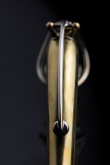 A raw brass neck of a saxophone on a dark background