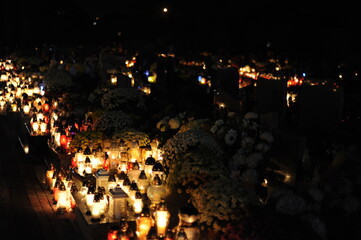 Candle lights on graves and tombstones in cemetery at night in Poland on All Saints’ Day or All Souls’ Day or Halloween or Zaduszki or Day of the Dead