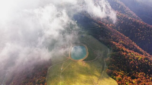 Aerial view of artificial lake in mountain, pine forest colored of autumn colors,dirty road,flying through the clouds fog above mountain tops.High peaks wonderful sunny autumn day,natural landscape