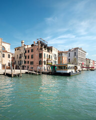 Grand Canal in Venice, Italy. Passenger vaporetto boat station and historic buildings on green water with blue sky. Venice water transport system. Water taxi system, logos removed for commercial use.