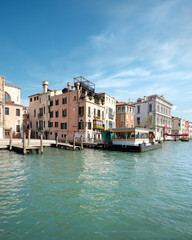 Grand Canal in Venice, Italy. Passenger vaporetto boat station and historic buildings on green...