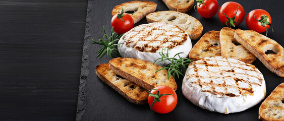 Grilled camembert, brie cheese with croutons, and cherry tomatoes on a dark background.