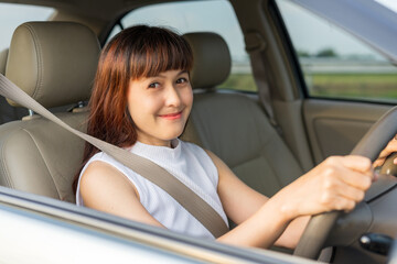Fototapeta na wymiar Happy female driver smiling while through car window. View of a lady driving her car to travel on her holiday vacation time. Loan car finance insurance, buy and rental concept.