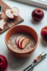 Freshly cooked oatmeal with apple pieces in a yellow bowl on the table. Morning nutritious breakfast.