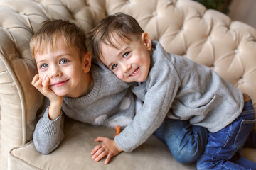 Two boys in New Year's sweaters lie upside down on the sofa and laugh. The concept of the new year