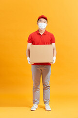 Delivery man employee in red cap blank t-shirt uniform face mask gloves hold cardboard box isolated on yellow background